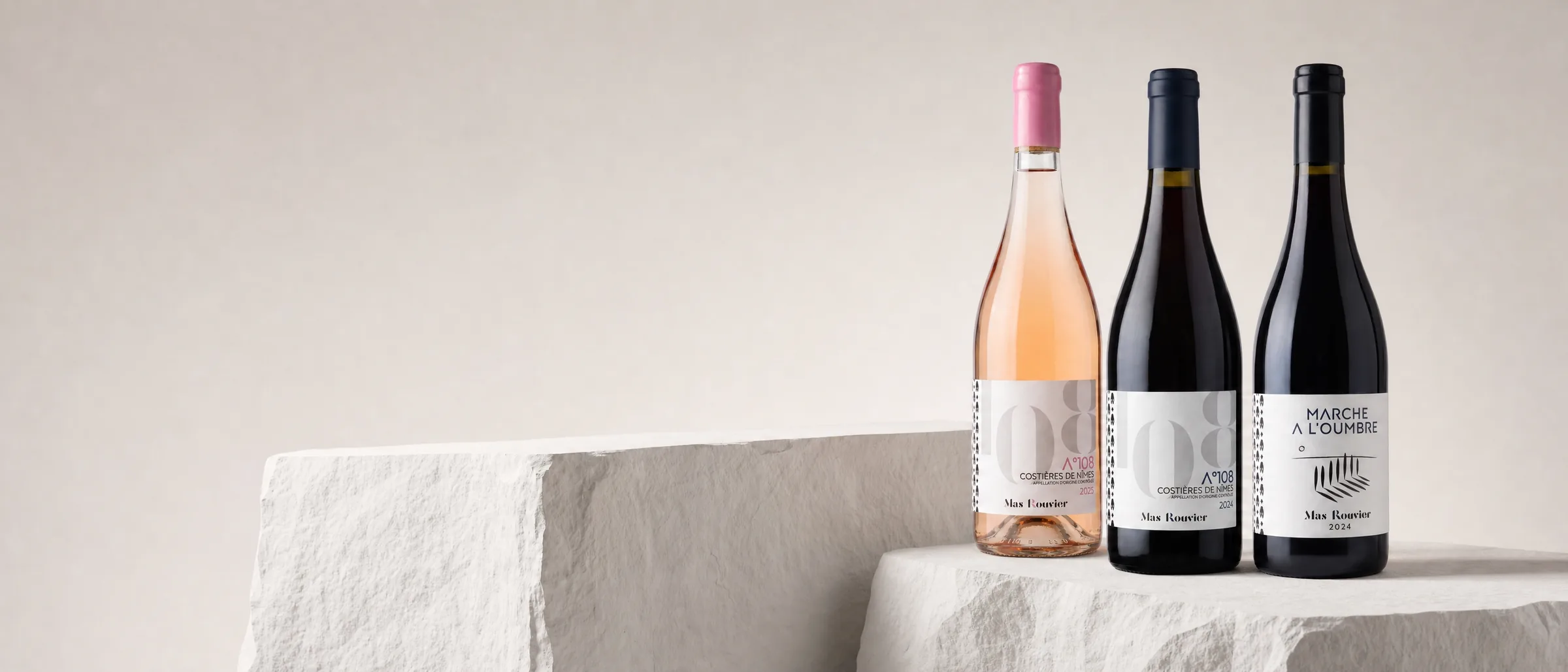 Les trois cuvées Mas Rouvier — A°108 rosé, A°108 rouge et Marche à l'Oumbre — posées sur des blocs de pierre